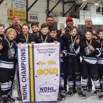 A North Bay Trapper's minor league hockey team on ice holding up a banner with "NDHL Champions" and "Pee Wee Gold" written on it
